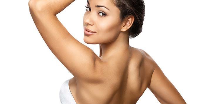 Close-up of a woman showing smooth underarm skin with a confident smile.