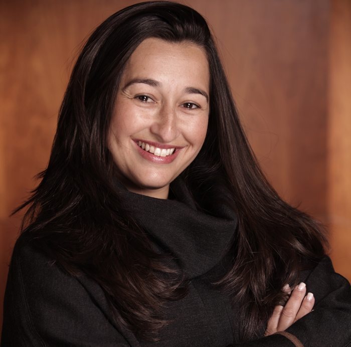 Smiling woman with long dark hair posing against a warm brown background.