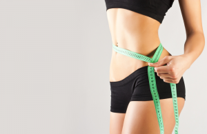 Woman measuring her slim waist with a green tape measure.